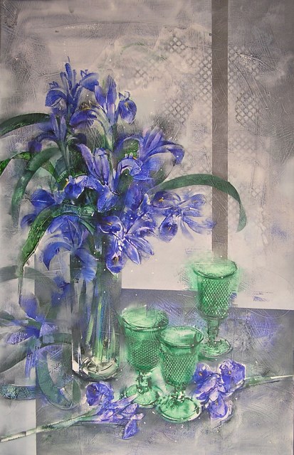 Lirios azules en un recipiente transparente junto a copas verdes sobre un fondo gris.