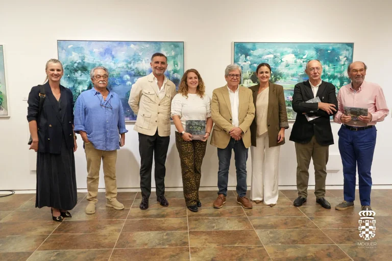 Pedro Rodríguez acompañado por asistentes a la inauguración, ante dos pinturas de invernaderos. Fotografía del Ayuntamiento de Moguer.