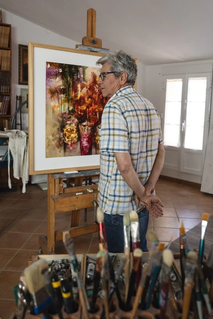 Pedro Rodríguez de pie junto a una pintura y materiales de trabajo en su estudio.