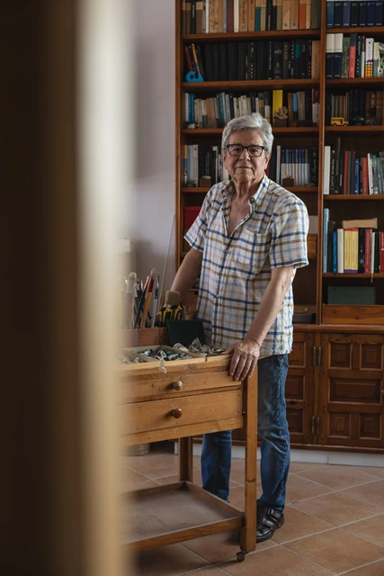 Pedro Rodríguez de pie en su estudio, junto a las estanterías y las obras.