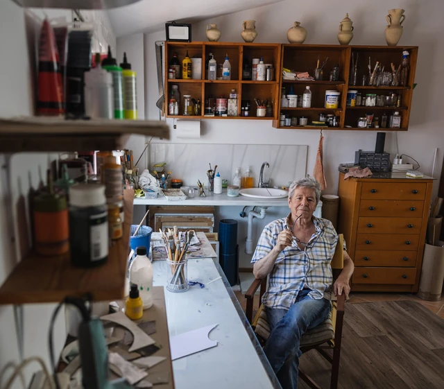 Vista del estudio de Pedro Rodríguez, con el artista sentado entre materiales, libros y pinturas.