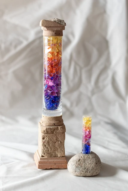 Dos formas cilíndricas transparentes con fragmentos de colores, sobre bases de distintas alturas.